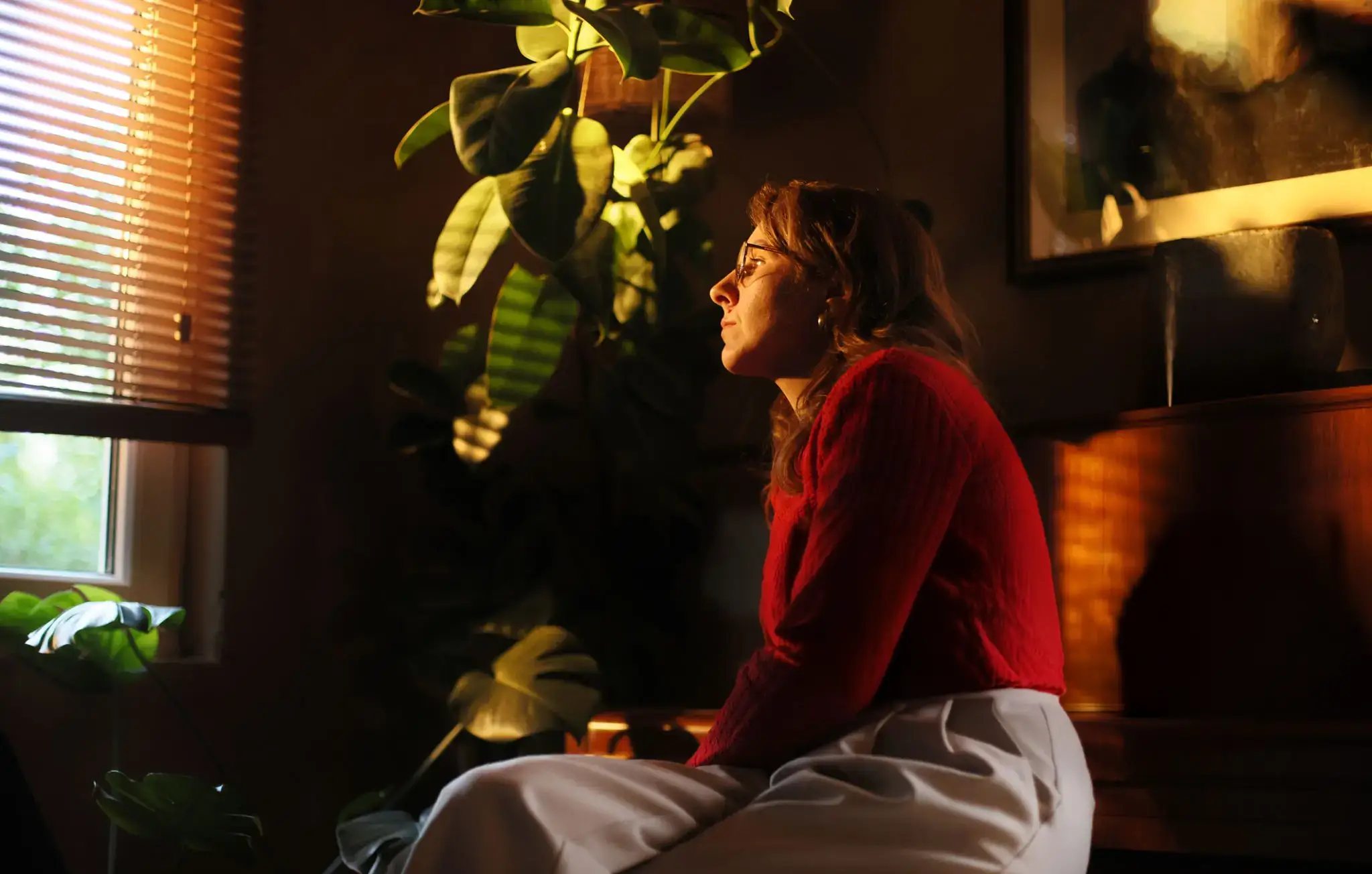 Woman on sofa looking out of a semi-closed blind into her garden.